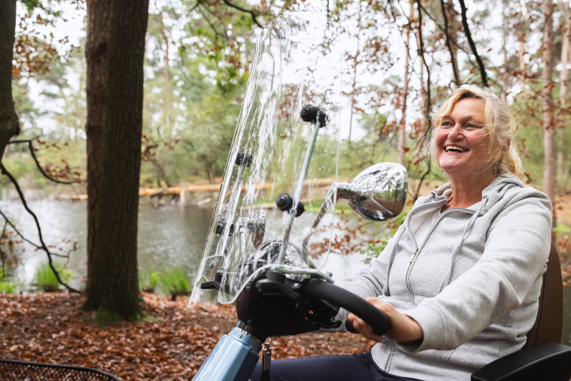 Een lachende vrouw rijdt op een scootmobiel langs het water.